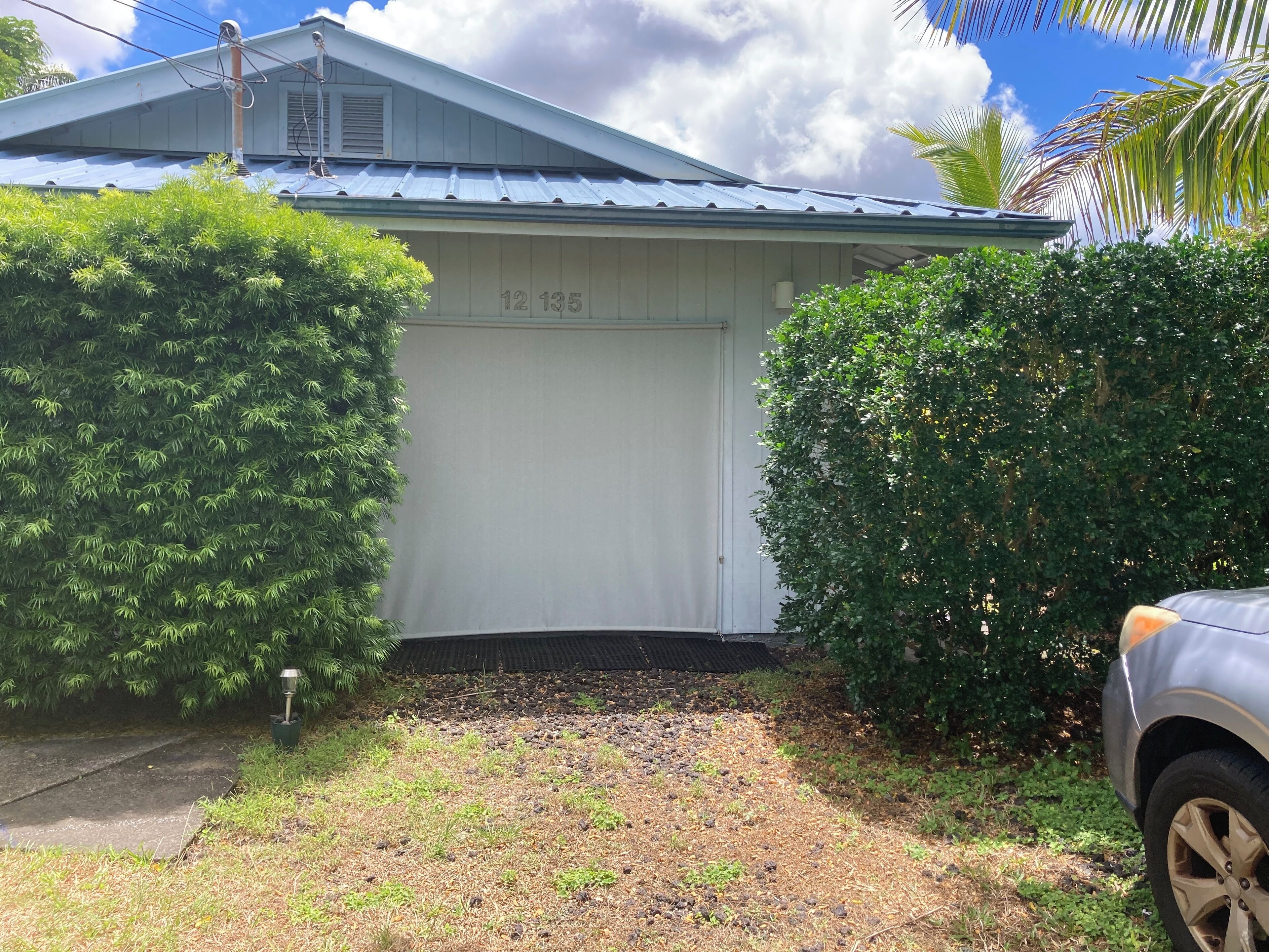 Un garage d’habitation dont la porte porte le numéro « 12 135 », entouré d’une végétation luxuriante et sous un ciel dégagé.