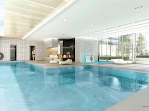 Une piscine intérieure au design moderne, un espace détente avec des canapés et une vue sur l’extérieur grâce à de grandes fenêtres.