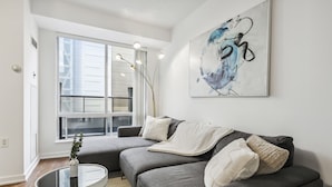 Un salon moderne avec un canapé gris, une table basse ronde et une grande fenêtre.