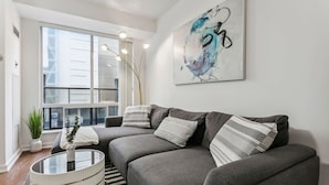 Un salon moderne avec un canapé d’angle gris, une table basse en verre et un grand tableau abstrait accroché au mur.