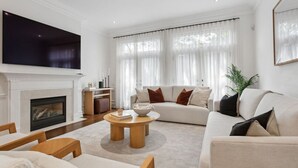 A living room with a fireplace, a large flat-screen TV, a sofa, and a coffee table. - Luxury Home Yorkville 4bed4bath Backyard Parking (Toronto)