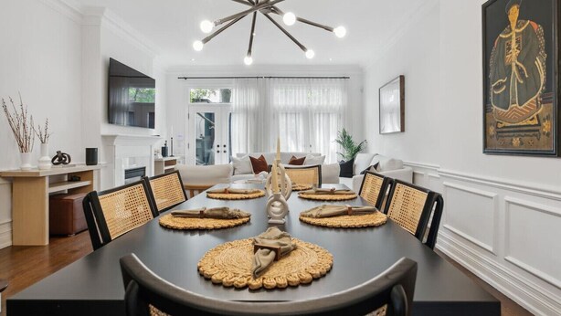A dining area with a dark table set for six, surrounded by wicker chairs, and a modern chandelier above. - Luxury Home Yorkville 4bed4bath Backyard Parking (Toronto)