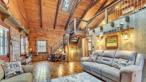 A spacious log cabin interior with a large sofa, a dining area, and a staircase leading to an upper level. - Family-Friendly Tyrone Cabin w/ Deck Near Hiking (Tyrone)
