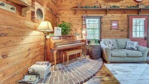A cozy cabin interior with a wooden piano, a sofa, a lamp, and a brick floor. - Family-Friendly Tyrone Cabin w/ Deck Near Hiking (Tyrone)