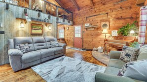 A cozy log cabin interior with a grey sofa, a piano, and a wooden staircase. - Family-Friendly Tyrone Cabin w/ Deck Near Hiking (Tyrone)
