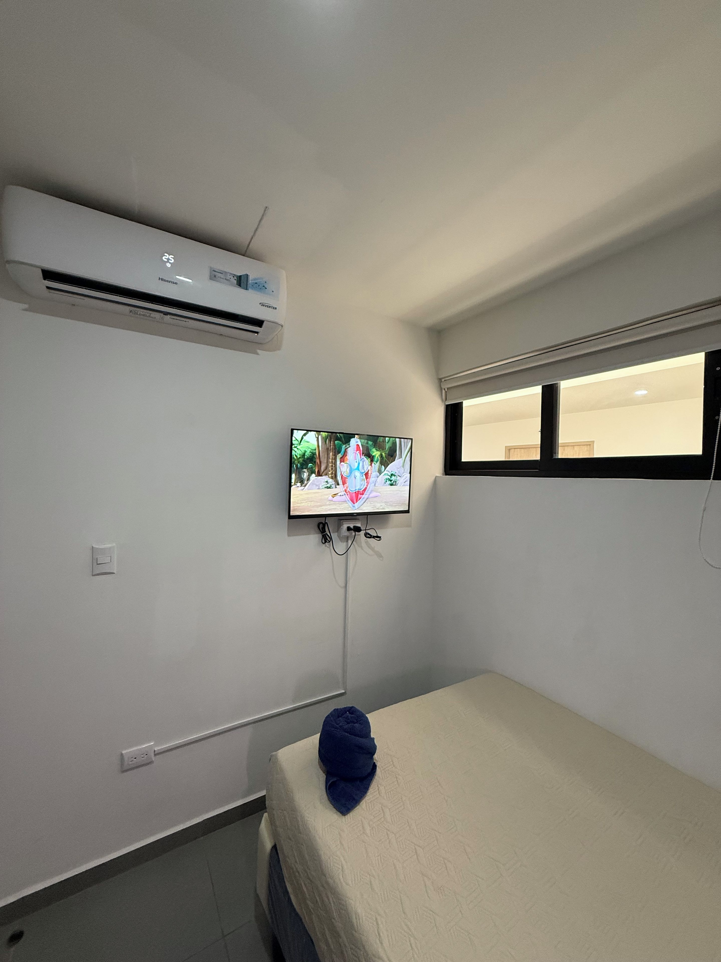 Ein Zimmer mit einem Bett, einer Klimaanlage, einem an der Wand montierten Fernseher und einem Fenster.
