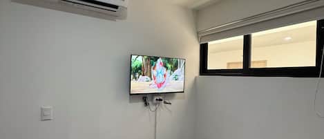Une chambre avec un lit, un appareil de climatisation, un téléviseur fixé au mur et une fenêtre.