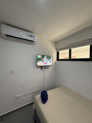 Quarto com cama, ar condicionado, televisão fixada na parede e janela.