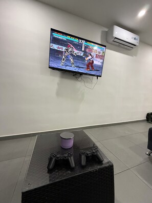 A television mounted on a wall displaying a video game, a black table with gaming controllers, and an air conditioning unit. - Apartment Escalon. 3 beds & 2 Sofa beds, WIFI, 2 car parking, AC in all bedrooms (San Salvador)