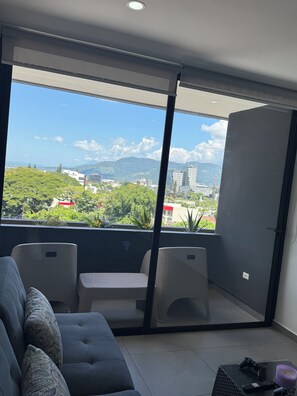 Uma varanda com sofá e cadeiras, vista para a cidade e céu claro.