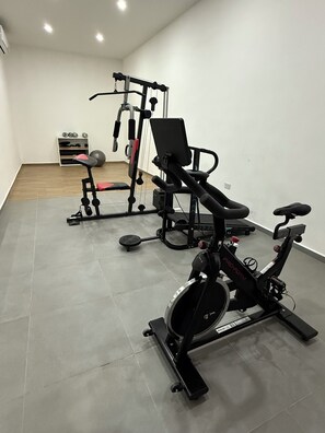 Uma academia em casa com uma bicicleta ergométrica, um banco de musculação e uma máquina de cabos.