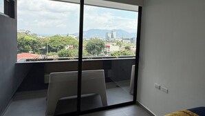 Ein modernes Zimmer mit einer großen Schiebeglasdoor zum Balkon, einem Bett mit gelber Tagesdecke und einem Sessel.