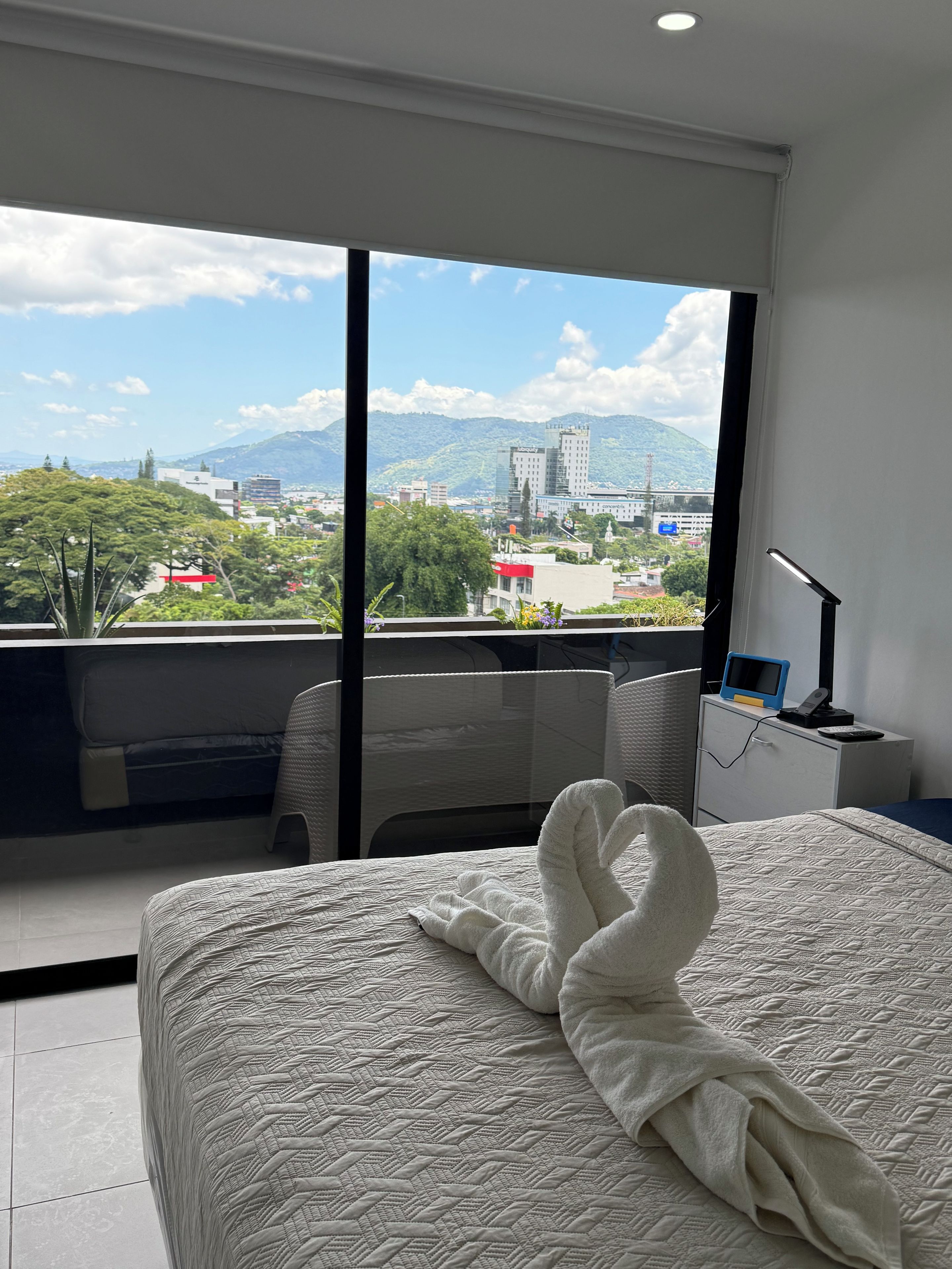 A hotel room with a large bed, a desk, and a view of a cityscape and mountains.
