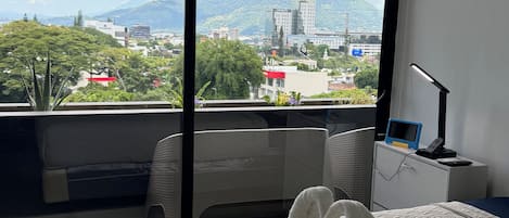 A hotel room with a large bed, a desk, and a view of a cityscape and mountains.