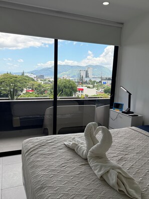 A hotel room with a large bed, a desk, and a view of a cityscape and mountains.