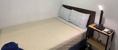 Uma cama de solteiro com cabeceira, uma mesa de cabeceira com abajur e uma janela com o número '401' na parede.