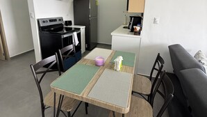 Eine kompakte Küche mit Herd, Backofen und Kühlschrank, ein Esstisch mit Stühlen sowie eine Couch.
