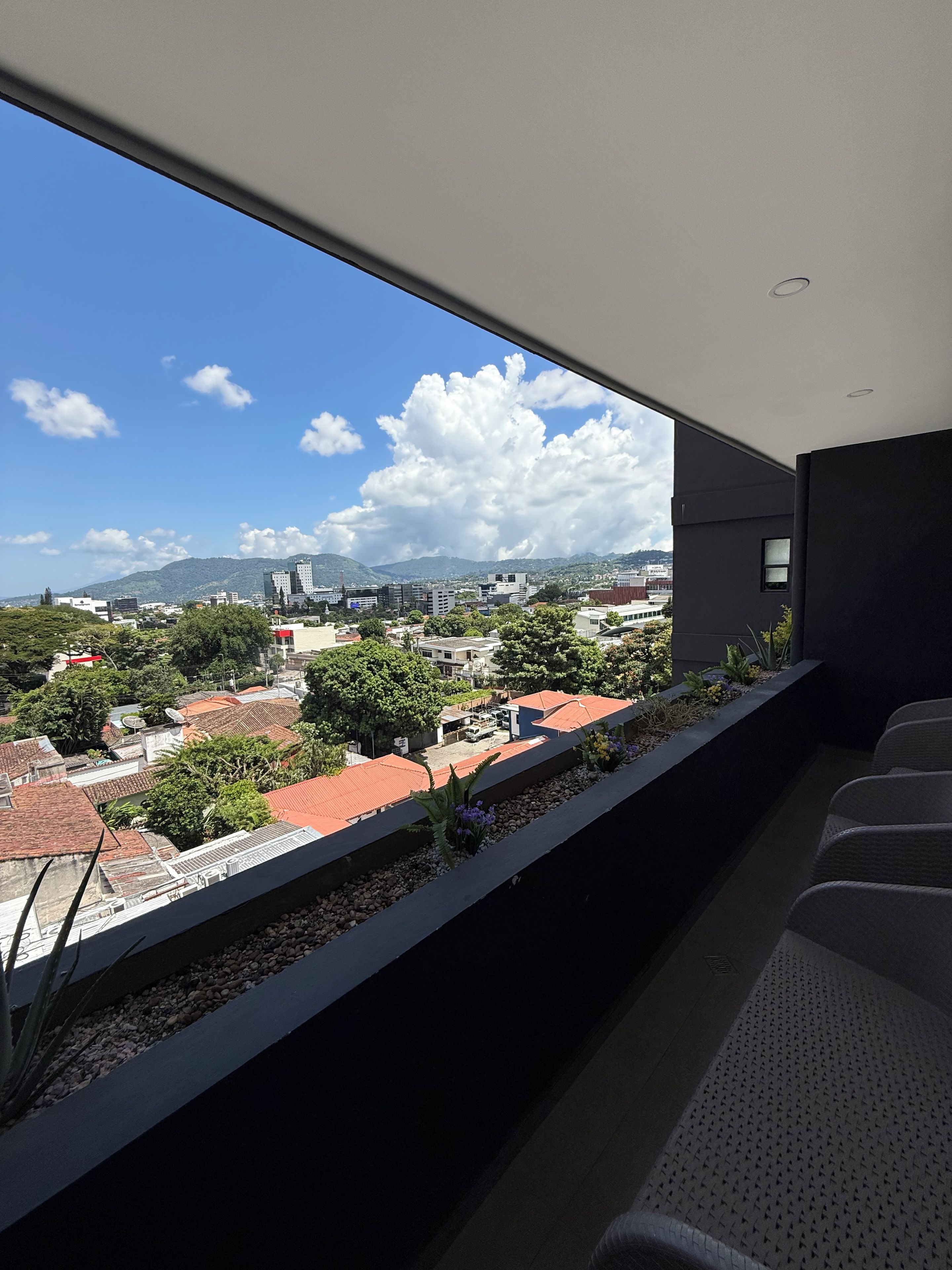 Un balcon offrant une vue sur le paysage urbain, avec des bâtiments et de la verdure.