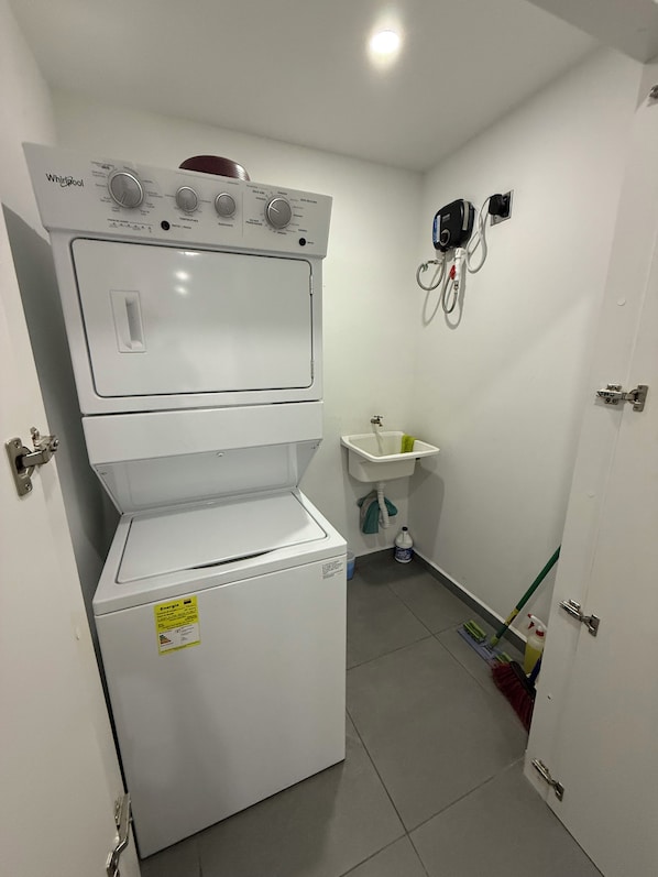 A compact laundry room with a stacked washer and dryer, a sink, and a mop.