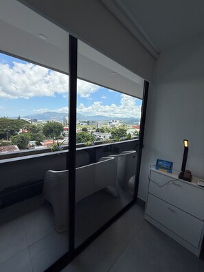 A balcony with a view of a cityscape and mountains, a white desk with a lamp, and a chair. - Apartment Escalon. 3 beds & 2 Sofa beds, WIFI, 2 car parking, AC in all bedrooms (San Salvador)