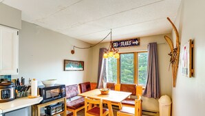 A compact kitchen with a dining area, featuring a wooden table, chairs, a microwave, and a stove. - Snow Mountain Condo: Hot Tub + Shuttle to Resort (West Dover)