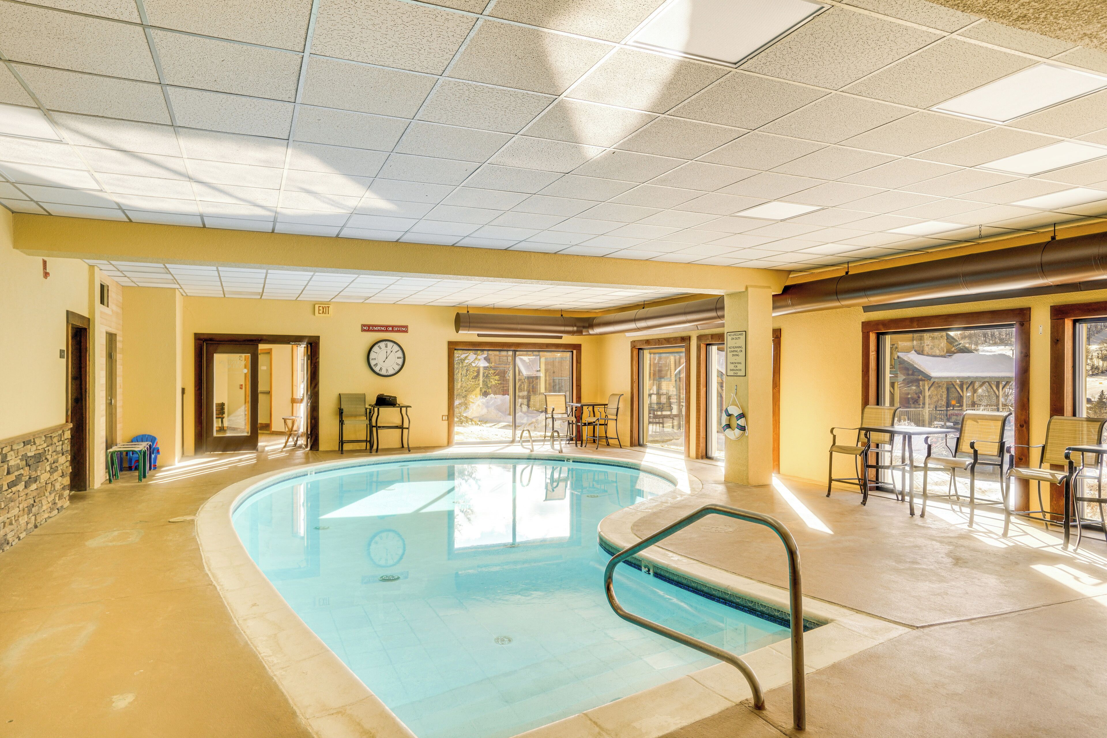 A pool area with a clock, chairs, and tables.