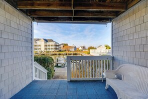 A covered balcony with a white wicker sofa and a view of a marina with boats and buildings.