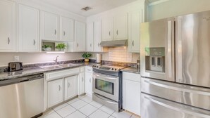 Een moderne keuken met witte kastjes, roestvrijstalen apparatuur en een marmeren aanrecht.