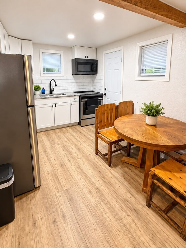 A compact kitchen with white cabinetry, a black refrigerator, a microwave, and an oven. There's a wooden dining table with chairs and a potted plant. - Cozy house in charming Anchorage with WiFi access (Anchorage)