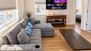 Een moderne woonkamer met een hoekbank, een flatscreen televisie en een salontafel met een geblokt patroon.