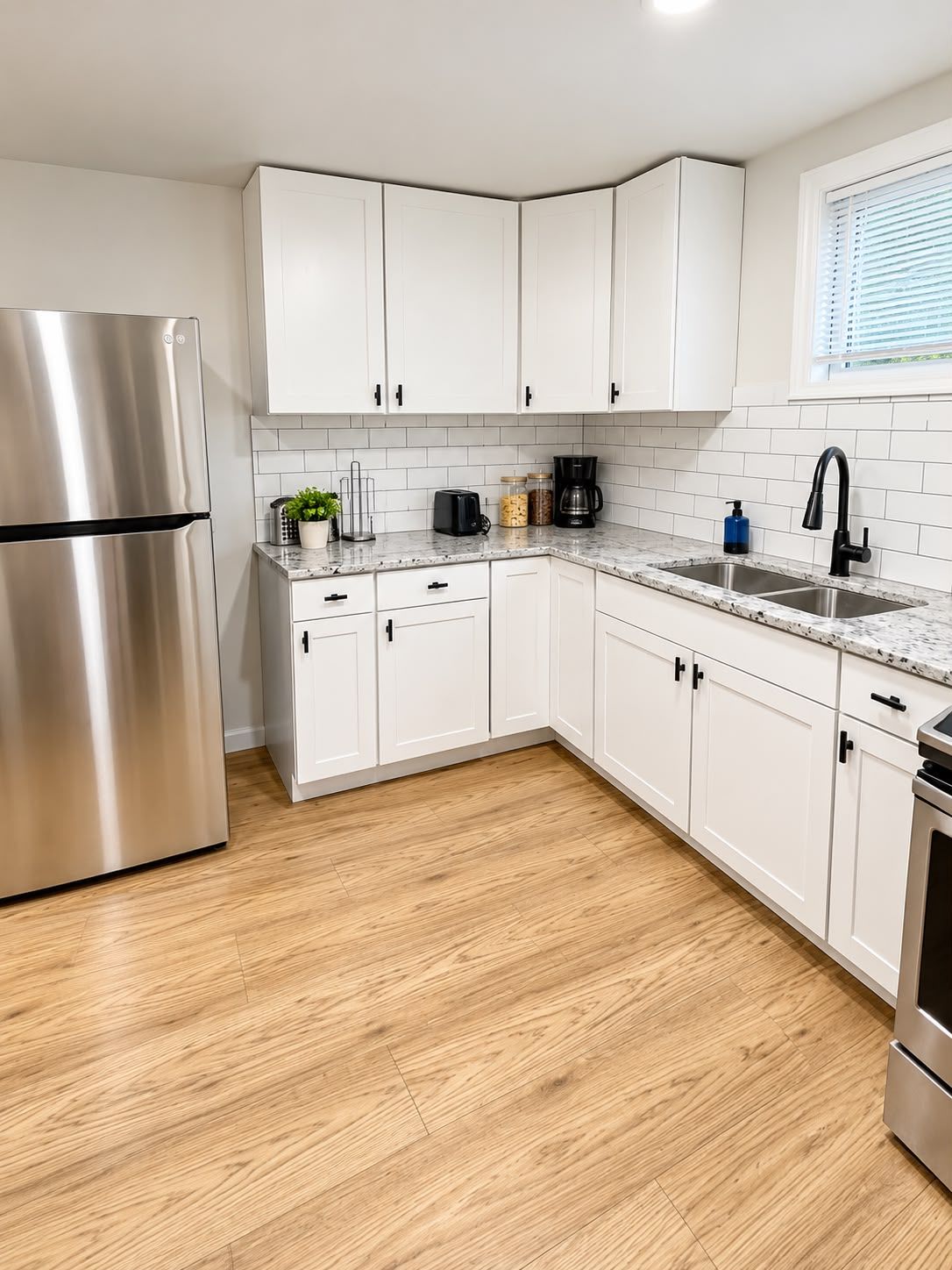 A modern kitchen with white cabinets, a stainless steel refrigerator, a coffee maker, and a sink.