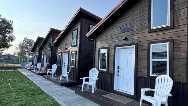 A row of cabins with white doors and windows, a concrete pathway, and a grassy lawn. - Glacier Alpine Lodges (East Glacier Park)