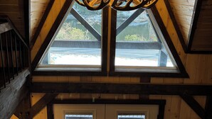 A room with a sloped wooden ceiling, a chandelier made of antlers, and a view through a large window. - Modern-Rustic, Secluded Cabin w/ Clarion River Frontage, Borders National Forest (Sigel)