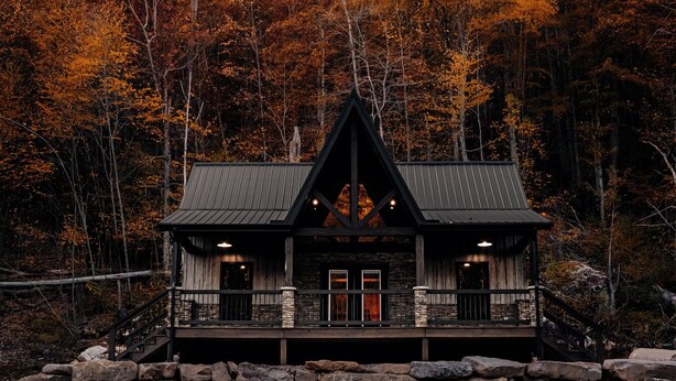 A lodge with a stone foundation, wooden exterior, and a metal roof, surrounded by autumn-colored trees. - Modern-Rustic, Secluded Cabin w/ Clarion River Frontage, Borders National Forest (Sigel)