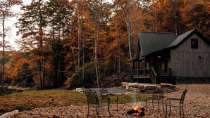A rustic cabin with a stone foundation, a wooden deck, and a fire pit in the foreground. - Modern-Rustic, Secluded Cabin w/ Clarion River Frontage, Borders National Forest (Sigel)