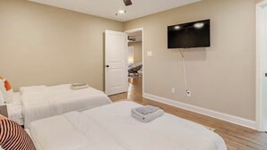 Habitación de hotel con dos camas, un ventilador de techo, un televisor montado en la pared y una puerta que da a otra habitación.