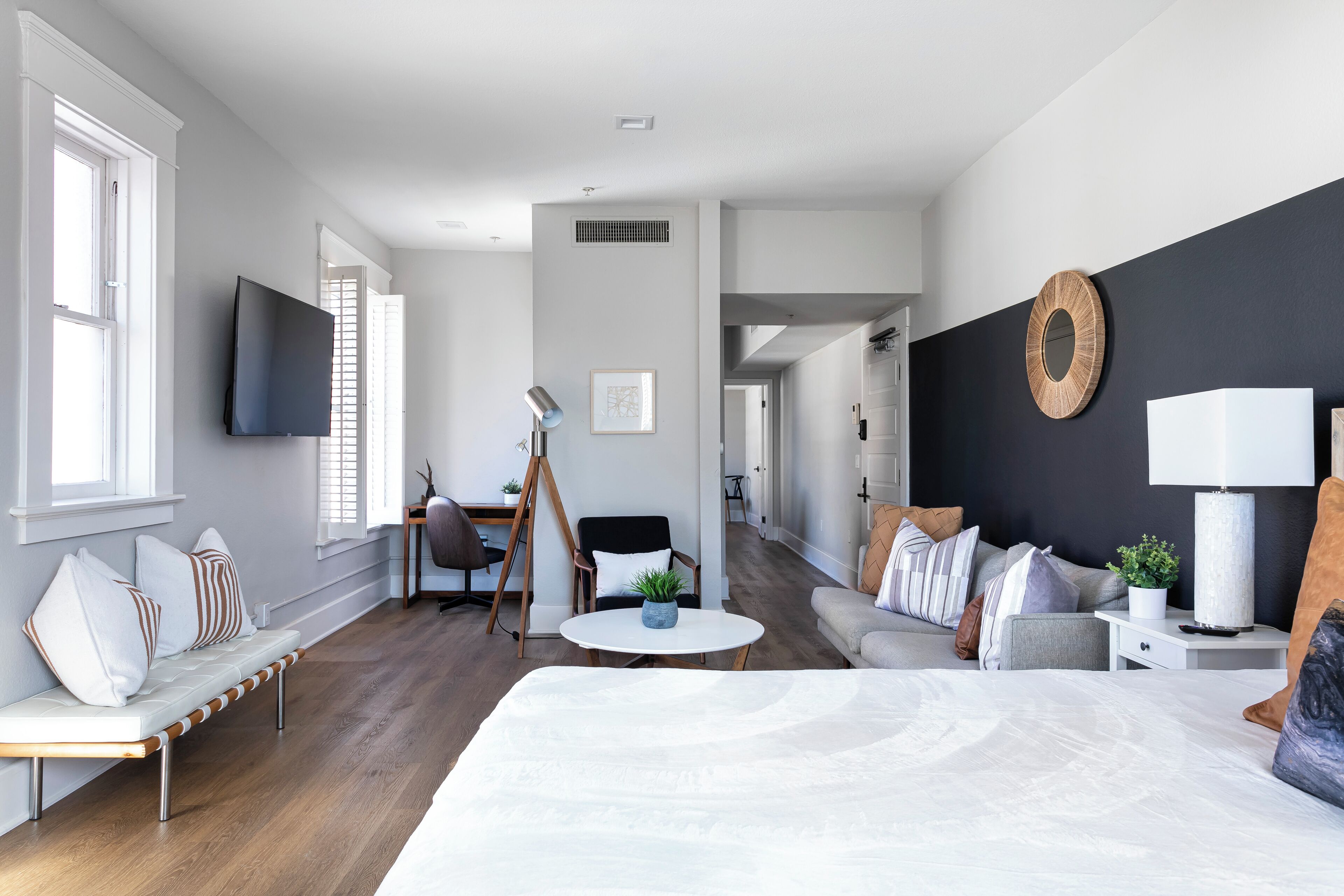 Une chambre d’hôtel moderne dotée d’un grand lit, d’un coin salon avec un banc et des fauteuils, d’une petite table ronde et d’un téléviseur fixé au mur.