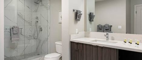 A modern bathroom with a glass shower enclosure, a white toilet, a vanity with a mirror, and a sink.