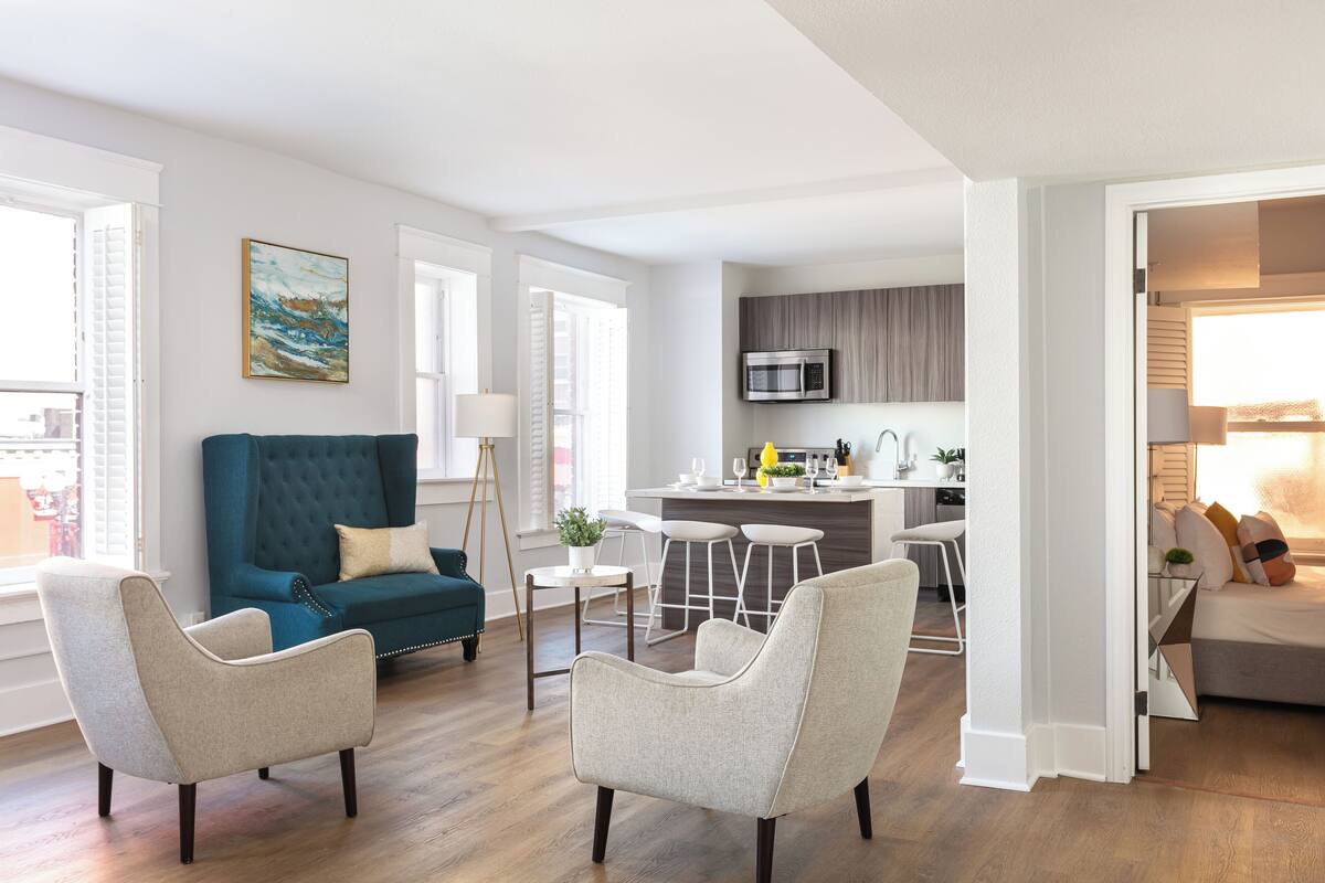 En moderne stue med blå sofa, to lænestole og et køkkenområde med mikrobølgeovn.