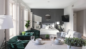 A modern bedroom with a bed, bedside tables, a TV, and a dining area with a table set for two.