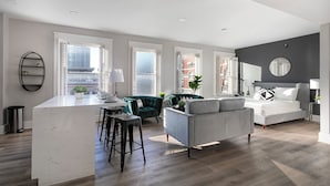 A modern apartment with a kitchen island, a grey sofa, a bed, and large windows with city views.
