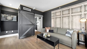 A modern living room with a grey sofa, a black coffee table, and a mounted dartboard.