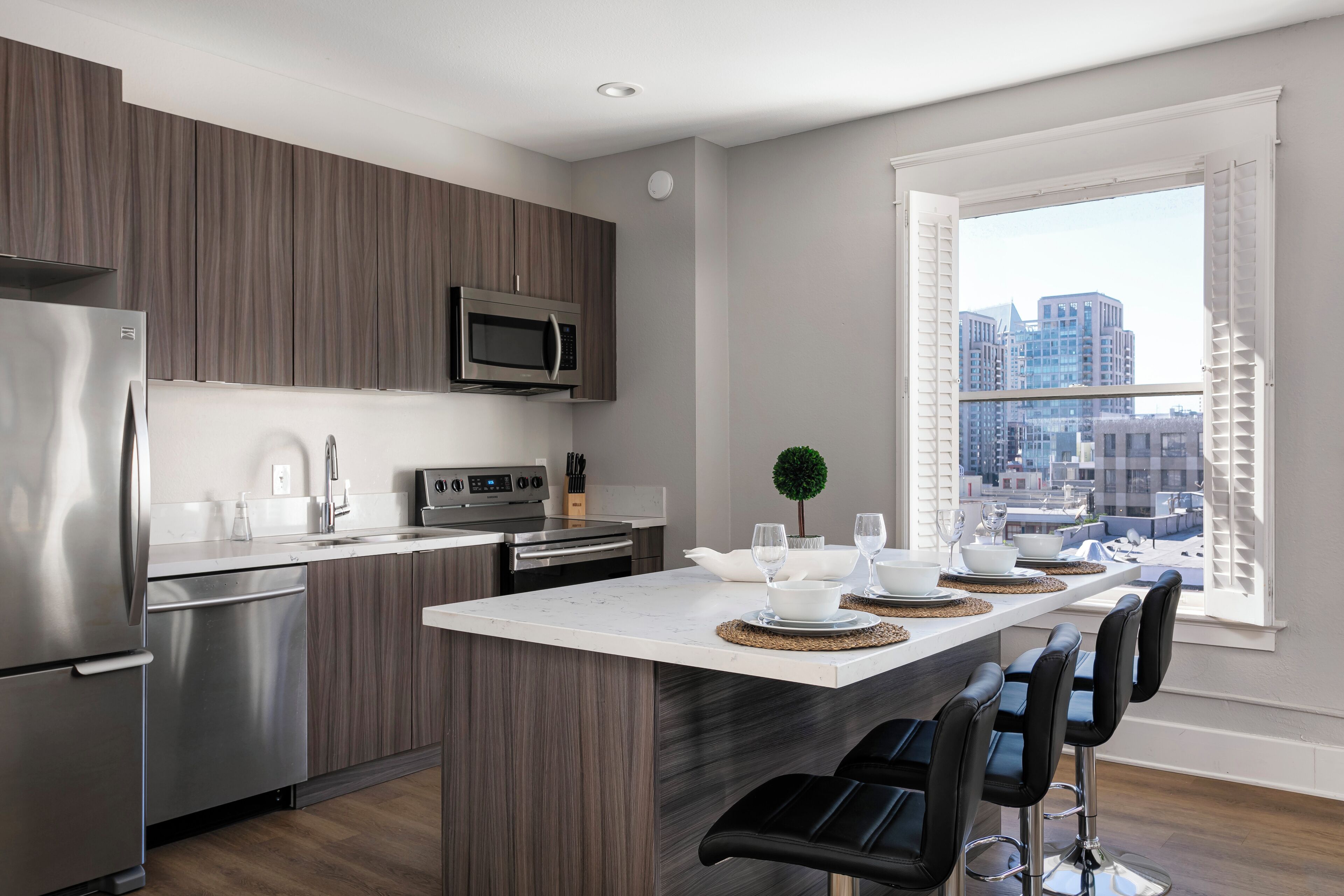 Una cocina moderna con una isla central, electrodomésticos de acero inoxidable y vistas de la ciudad a través de un ventanal amplio.