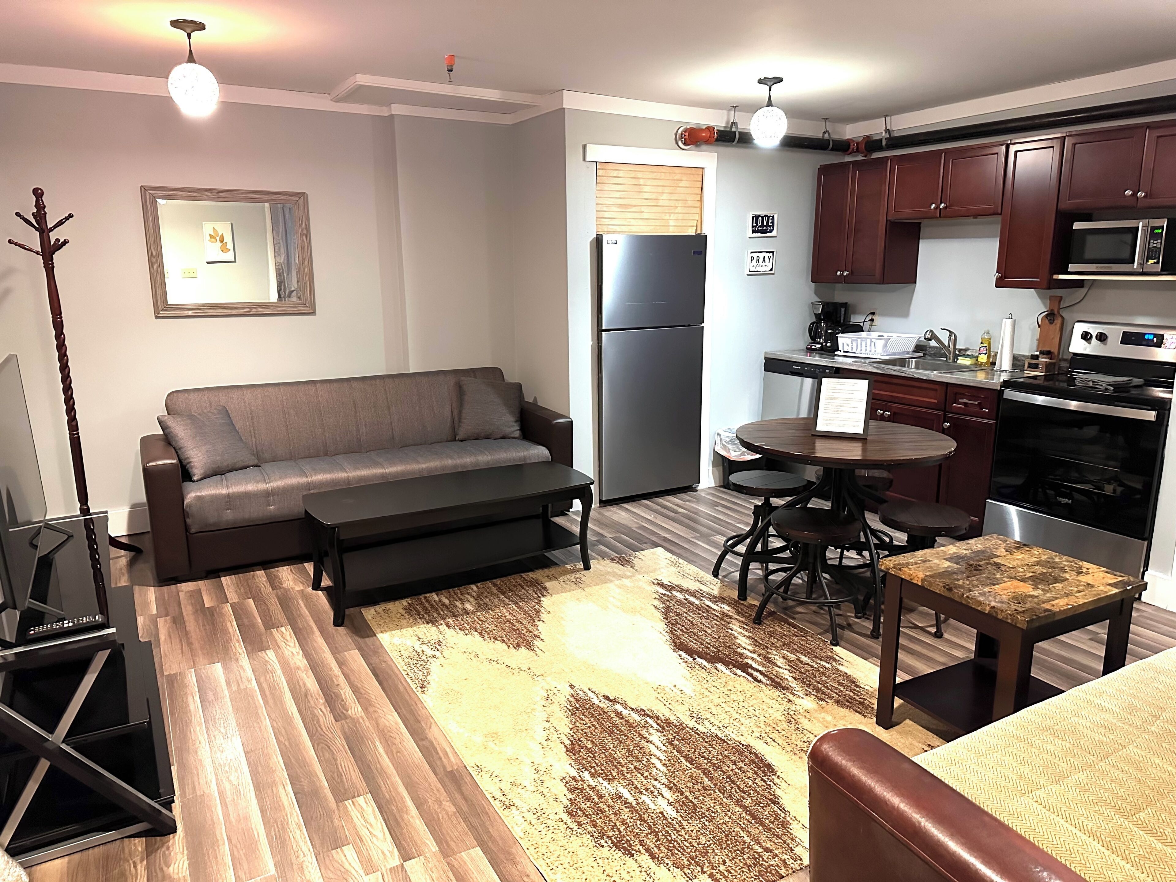 A compact living space with a sofa, coffee table, and a dining area with a table and chairs. A kitchen with appliances and cabinets is visible.