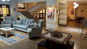 A modern living room with a sofa, armchairs, a coffee table, and a patterned rug. There is a staircase leading to another level, a dining area with a table and chairs, and a wall with a decorative light fixture. - Heritage valley. (New Cairo 1)