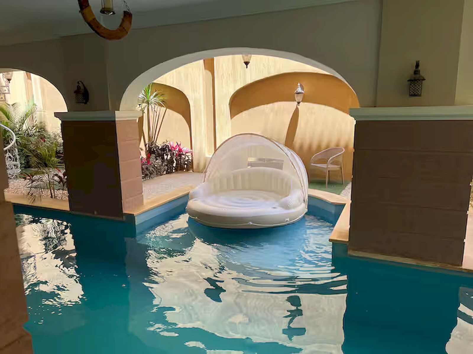 A swimming pool with a clear water feature, a lounge chair, and a small table.