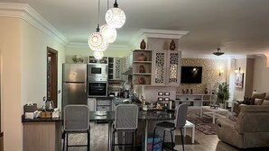 A modern kitchen with a dining area, a living room, and a TV mounted on the wall. - Heritage valley. (New Cairo 1)