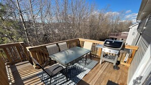 A wooden deck with a table and chairs, a grill, and a view of trees and a house in the background. - Spacious 4BR Boho - Family + Pet Friendly (Clarksville)