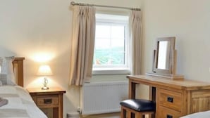 A bedroom with a bed, bedside table, lamp, window with curtains, radiator, and a wooden desk with a chair.