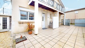 A residential building with a tiled patio, a balcony, and a potted plant.